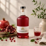 Main-Feines Granatapfel Likör – fruchtiger Likör mit Granatapfel Flasche Main-Feines Granatapfel Likör mit frischen Granatäpfeln, Granatapfelkernen und dezentem hellem Hintergrund