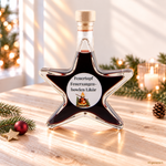 Feuertopf Feuerzangenbowlen-Likör in weihnachtlicher Sternflasche Feuertopf Feuerzangenbowlen-Likör in einer Sternflasche auf hellem Naturholztisch mit Tannenzweig, goldenem Stern, roter Weihnachtskugel und warmem Fensterlicht.