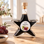 Aceto Superiore Balsamico Sternflasche Feinkost-Geschenkflasche – Geschenkidee Sternflasche Feinkost-Geschenkflasche mit Aceto Balsamico Superiore (3% Säure) in weihnachtlicher Deko-Szene mit frischem Rosmarin und Weintrauben – perfekt als Feinkost-Geschenk, Mitbringsel oder Firmenpräsent für Genießer