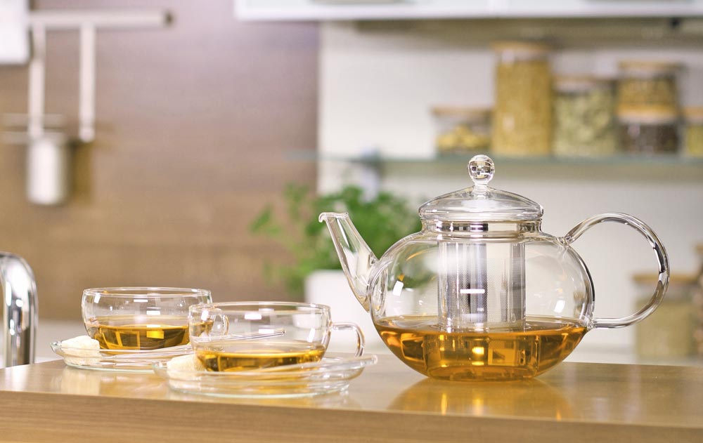 Teekanne mit Edelstahlfilter und zwei Teetassen aus Glas auf einer Küchenarbeitsplatte