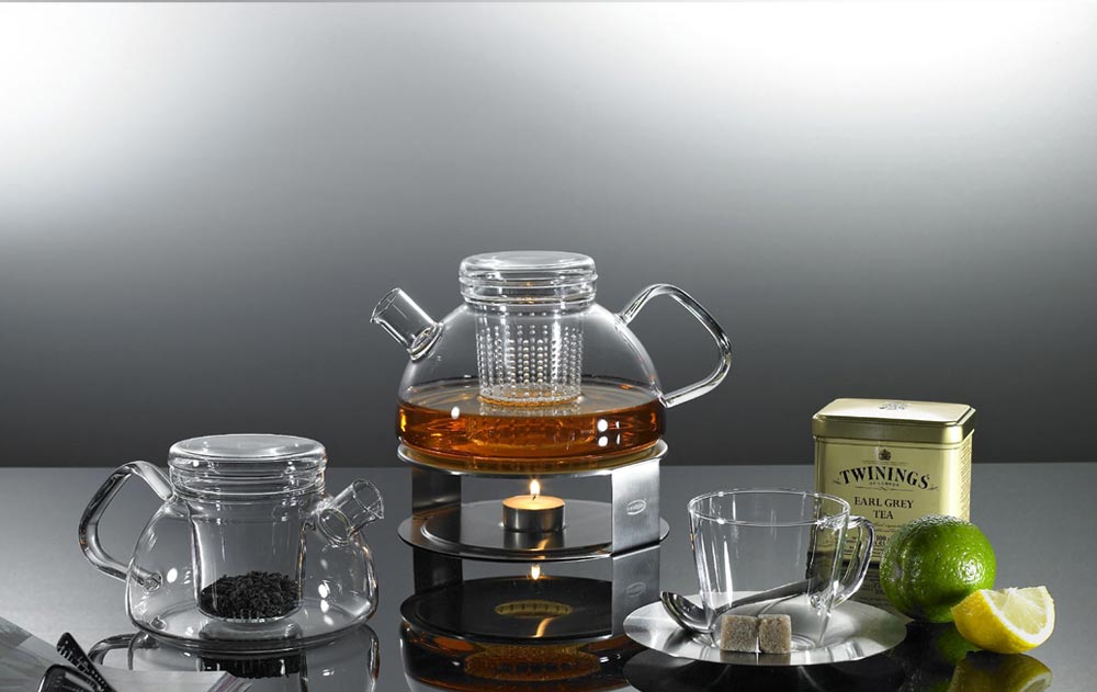 Teekanne auf einem Stövchen mit Teelicht, daneben eine kleine Teekanne mit Glasfilter, Teetasse, Teedose und Limette