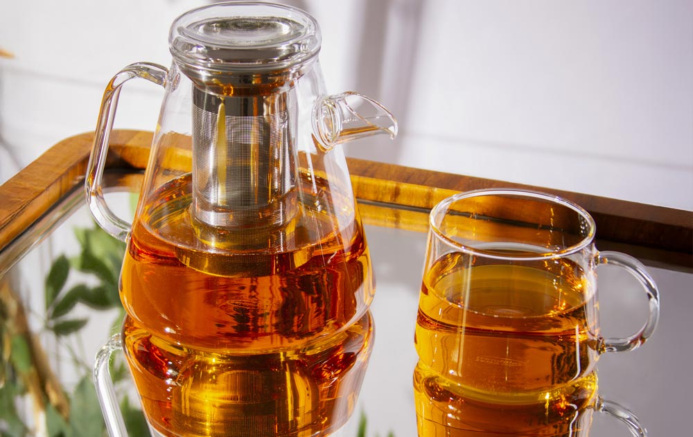 Teekanne mit Edelstahlfilter und Teebecher aus Glas, beide mit Tee gefüllt