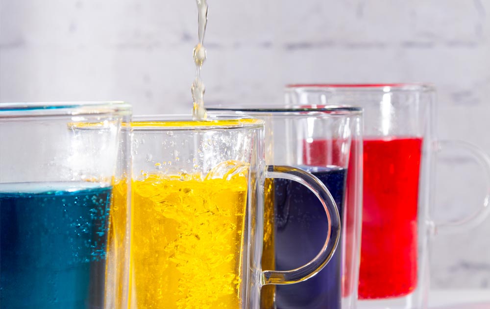 Doppelwandige Gläser mit blauer, gelber und roter Flüssigkeit, in eines wird eingeschenkt