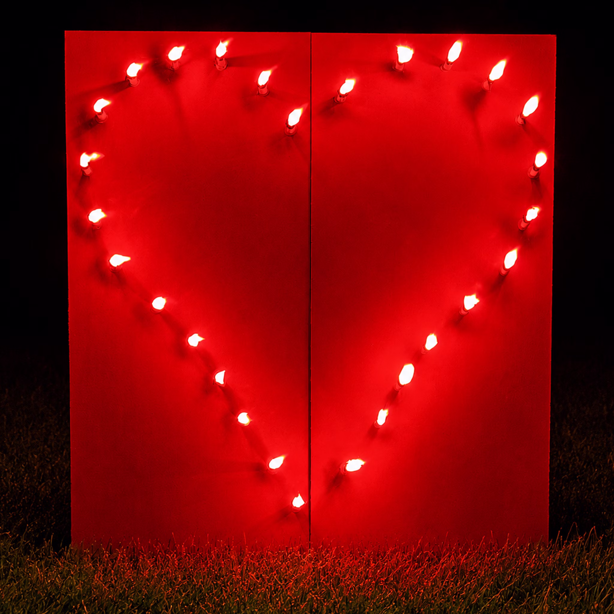 Lichterbild Brennendes Rotes Herz auf einer Wiese bei Dunkelheit.