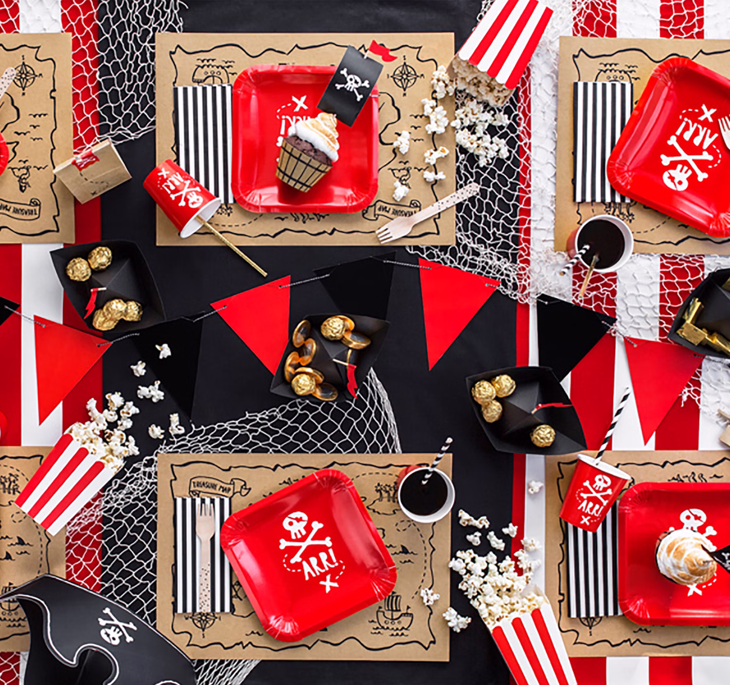 Piratenparty-Tischdekoration mit roten Tellern, schwarz-weißen Papierstrohhalmen, Schatzkarten-Platzsets und maritimen Dekoelementen.