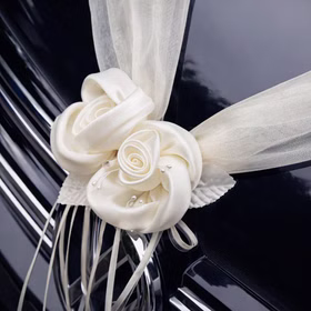 Detailansicht zweier cremefarbener Rosenblüten aus Satinoptik mit transparentem Organza und dekorativen Schleifenbändern auf einer glänzenden Motorhaube.