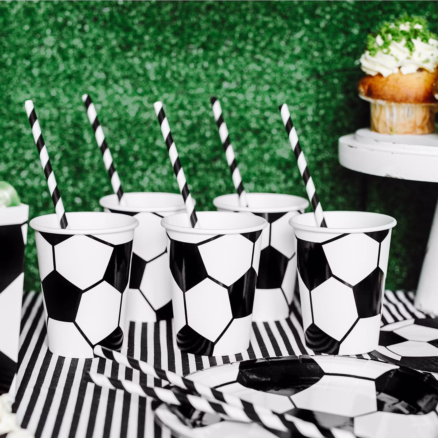 Fußballbecher mit schwarz-weißen Papierstrohhalmen auf dekoriertem Partytisch.