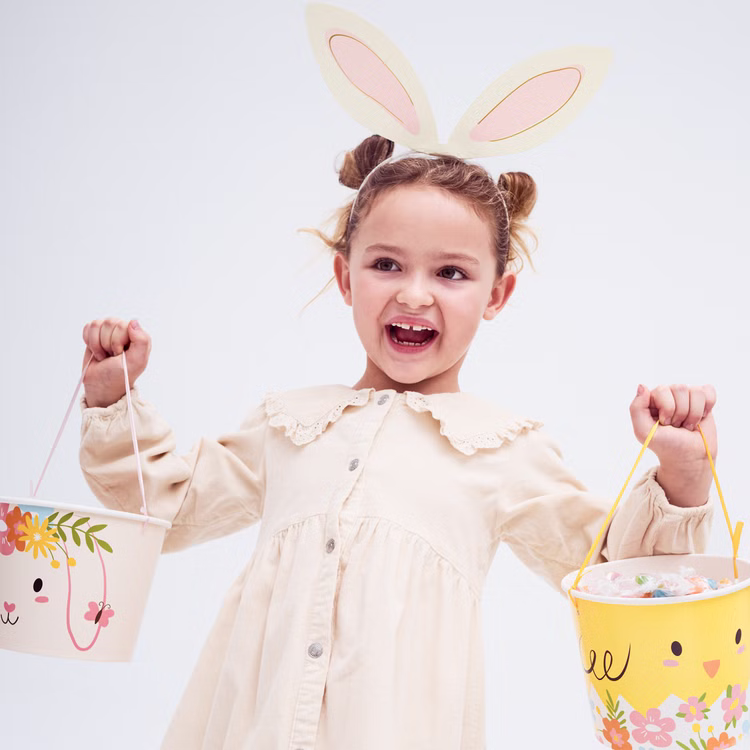 Hasenohren Haarreif Bastel-Set 4 Stück DIY Osterohren Rosa Creme Ostern SALE Hasenkostüm Oster-Deko Oster-Basteln Kindergeburtstag Fasching Karneval und Mottopartys Mädchen mit selbst gestalteten Hasenohren hält zwei Osterkörbchen voller Süßigkeiten in den Händen.