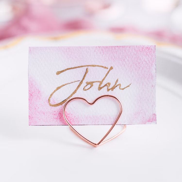 Tischkartenhalter Herzen Roségold 10 Stück Platzkartenhalter Hochzeit Geburtstag SALE Fotohalter Rosé Tischdeko Taufe Jugendweihe Kommunion Tisch-Deko Dekoration Zubehör Roségoldener Herzhalter präsentiert eine beschriftete Platzkarte als stilvolle Tischdekoration.