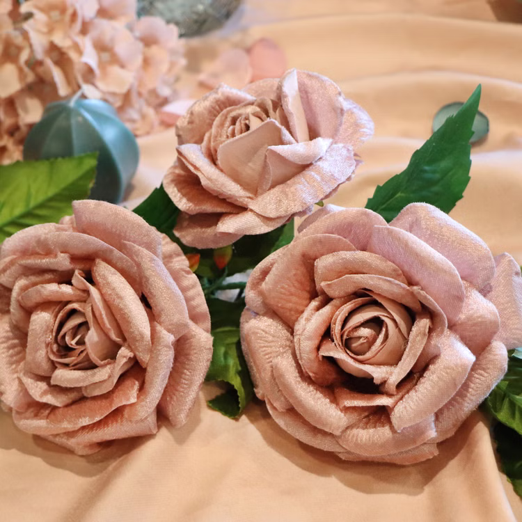 Rosen Girlande Tischdeko Luxus Rosen Puderrosa Samt 20 cm x 2 m Deko Hochzeit Tischdeko Deko-Ideen Geburtstag festliches Ambiente Nahaufnahme von drei altrosa Rosenblüten mit grünen Blättern auf Stoffunterlage.