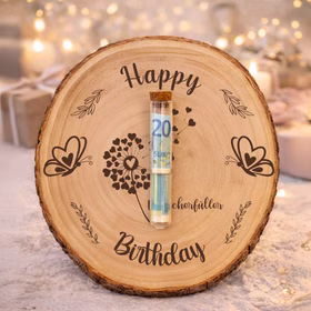 Baumscheibe 24 cm Happy Birthday Wunscherfüller Geldgeschenk Individuelles Geschenk DIY-Geschenkidee Geburtstag Holzscheibe Bastelbedarf Basteln Baumscheibe mit „Happy Birthday“-Gravur und Wunscherfüller-Motiv, dekoriert mit einem mittig befestigten Reagenzglas mit Geldschein, stimmungsvoll arrangiert in festlicher Geburtstagsdekoration mit Kerzen und Geschenken.