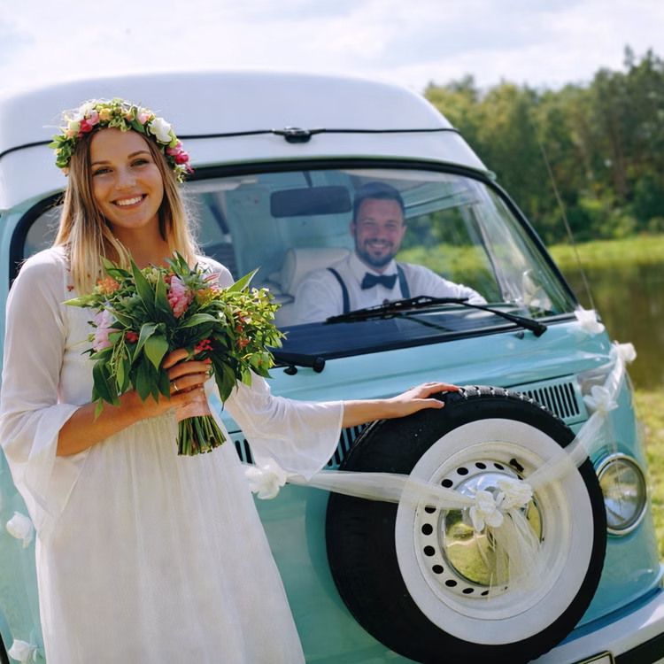 Autoschmuck Deko 2 Girlanden mit Blüten Weiß 180 cm Motorhaube Hochzeitsauto Wedding Car Organza-Girlande mit Rosenblüten Dekoration Braut mit Blumenstrauß steht vor einem hellblauen Hochzeitsauto, das mit weißen Organza-Girlanden geschmückt ist.