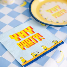 Minions Serviette Yay Party Tischdeko Minions Yay-Party-Serviette als Tischdekoration auf der blau karierten Tischdecke neben einem gelben Pappteller.