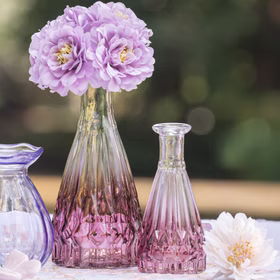 Große und kleine Glasvase mit rosa Farbverlauf, jeweils mit Blumen bestückt, dekorativ auf einem Tisch im romantischen Stil platziert.