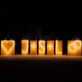 Lichterbilder Lichterbild Brennende Buchstaben Feuerwerk Geschenkidee Geburtstag Goldene Hochzeit Jubiläum Brennendes Hochzeits-Lichterbilder mit Herz, Initialen und Ringen auf goldenen Tafeln bei Nacht im Freien aufgebaut.