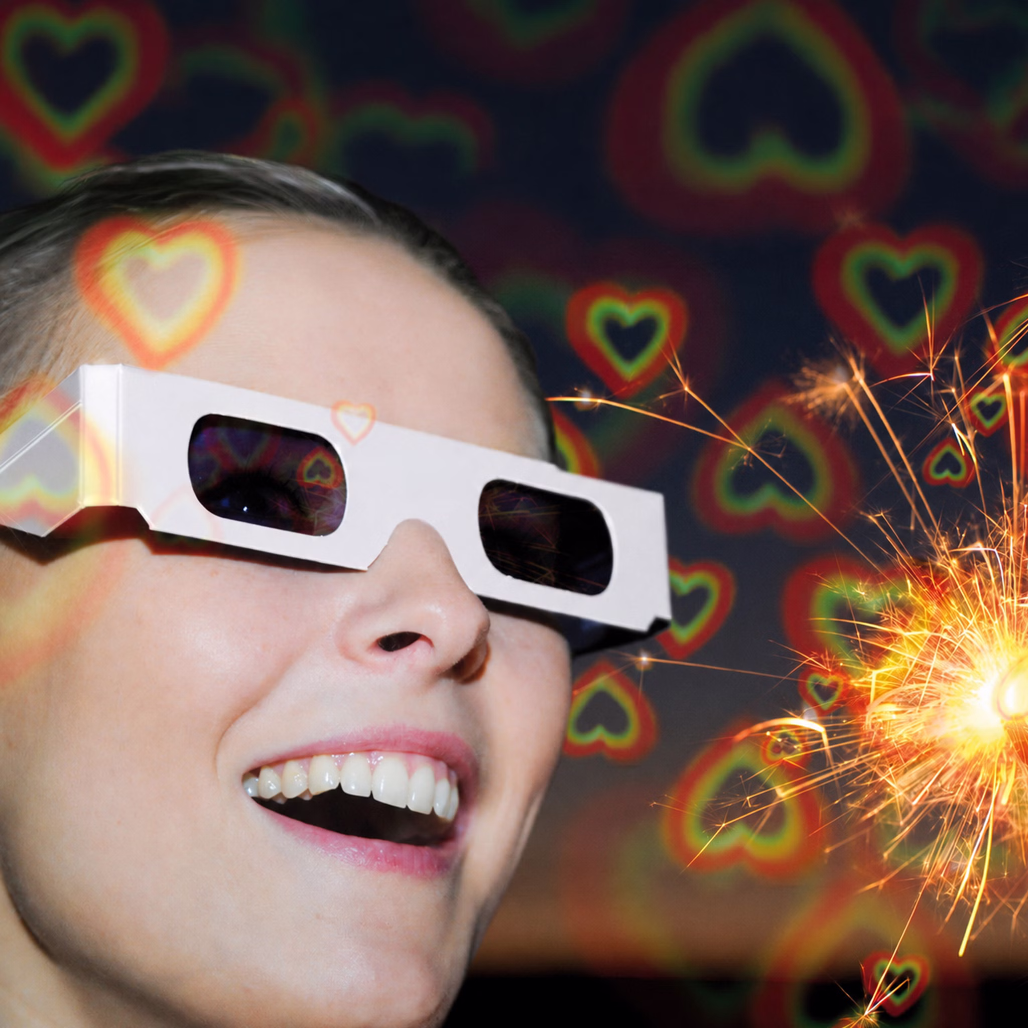 Frau mit weißer Effektbrille betrachtet eine Wunderkerze; farbige Herzformen zeigen den sichtbaren Lichteffekt der Brille.