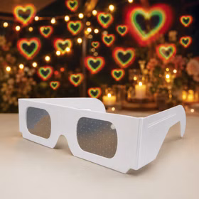 Weiße Effektbrille auf einer festlich gedeckten Tafel; leuchtende Herzformen im Hintergrund zeigen den romantischen Lichteffekt.