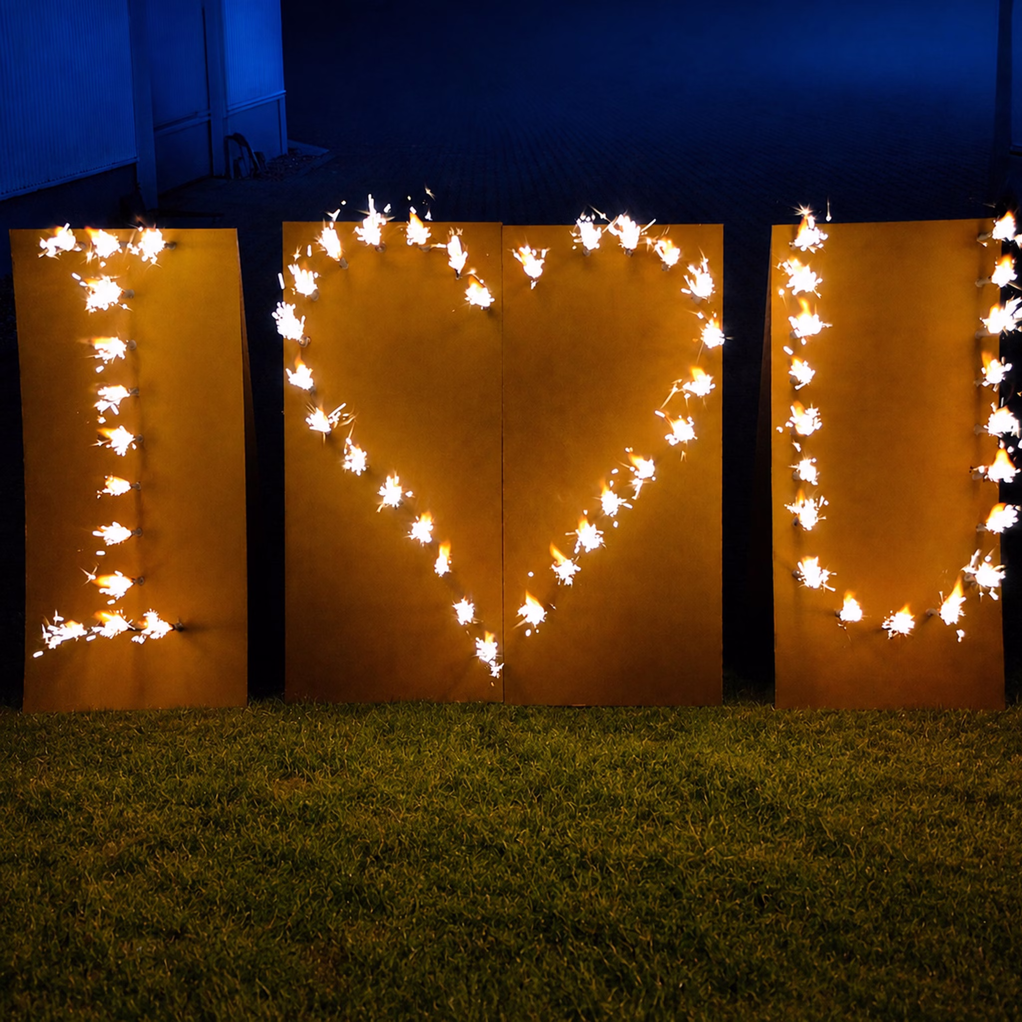 Lichterbild Brennendes Herz I love U auf grünem Rasen bei Dämmerung.