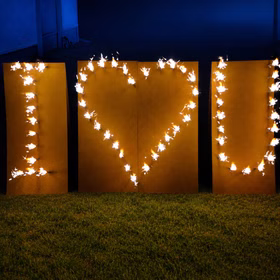 Lichterbild Brennendes Herz I love U auf grünem Rasen bei Dämmerung.