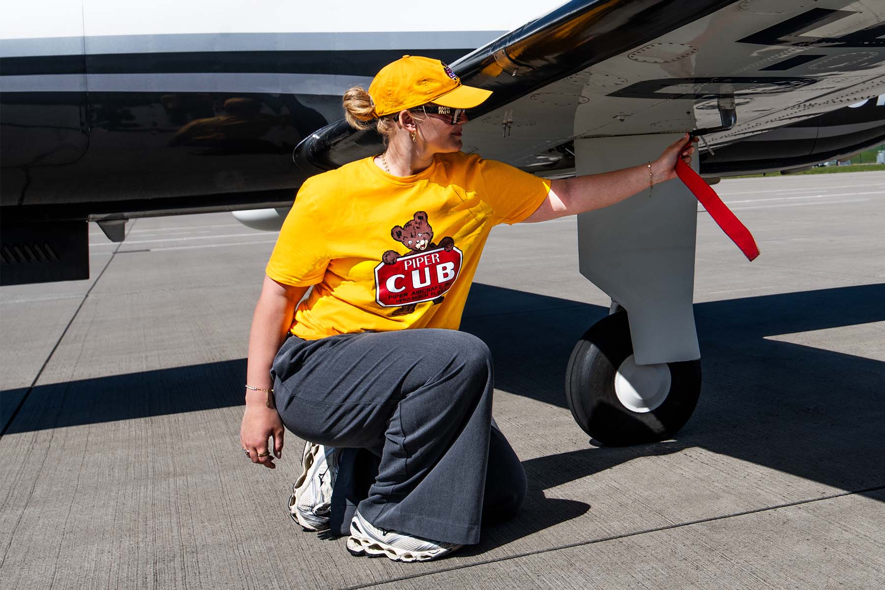 Eine Frau einem gelben Piper CUB T-Shirt kniet vor einem Piper M700 