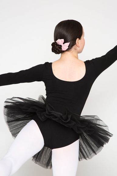 Eine junge Balletttänzerin in einem schwarzen Ballettbody und Tutu und mit einer rosa Schleife im Haar posiert.