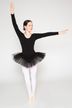 Eine junge Ballerina in einem schwarzen Tutu und weißen Strumpfhosen posiert mit erhobenen Armen in einer Ballettposition. 3