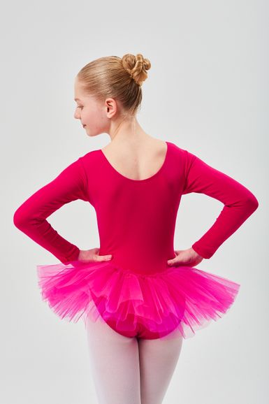 Eine junge Balletttänzerin in einem rosa Ballettbody und Tutu steht mit den Händen in den Hüften und blickt von der Kamera weg.