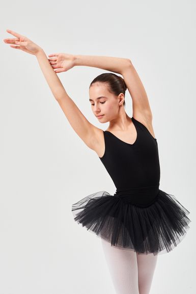 Eine junge Balletttänzerin in einem schwarzen Ballettbody und Tutu posiert mit anmutig ausgestreckten Armen.