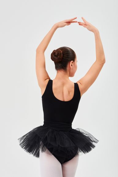 Eine Balletttänzerin in einem schwarzen Ballettbody und Tutu posiert mit erhobenen Armen.