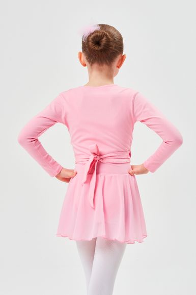 Ein junges Mädchen in einem rosa Ballett-Outfit steht mit den Händen in den Hüften und blickt von der Kamera weg.