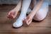 Kind in Ballettkleidung bindet die Bänder an einem weißen Ballettschuh 6