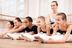 Fünf junge Ballettschülerinnen dehnen sich unter Aufsicht ihrer Lehrerin auf dem Boden eines Tanzstudios. 7