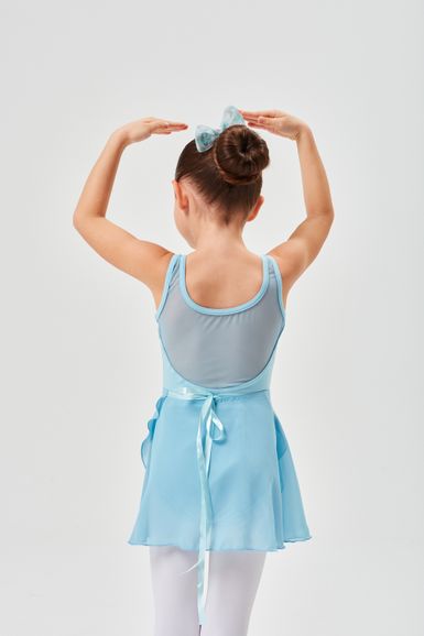 Ein junges Mädchen in einem blauen Ballett-Outfit steht mit erhobenen Armen vor einem schlichten Hintergrund