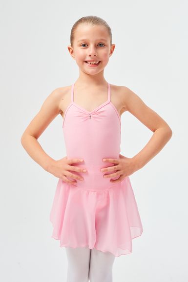 Ein junges Mädchen in einem hellrosa Ballettkleid steht lächelnd mit den Händen in den Hüften.