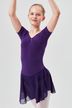 Eine junge Person in einem lila Ballettbody und Rock posiert mit erhobenen Armen. 1