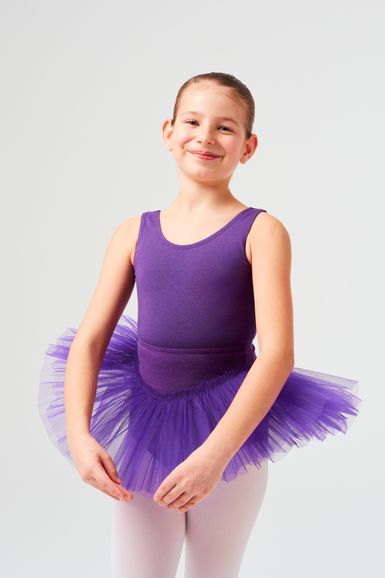Ein junges Mädchen in einem lila Ballettbody und Tutu steht mit ausgestreckten Armen da und lächelt.