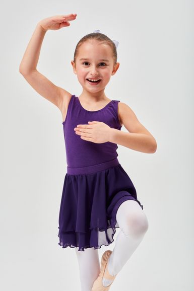 Ein junges Mädchen in einem lila Ballettbody und Tutu posiert in einer Balletthaltung mit einem erhobenen Arm und einem angehobenen Bein.