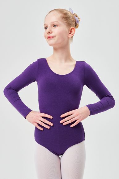 Ein junges Mädchen in einem lila Langarmbody und weißen Strumpfhosen steht mit den Händen in den Hüften und schaut zur Seite.