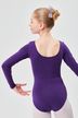 Ein junges Mädchen in einem lila Ballettbody und einer Schleife steht in einer Ballettpose und blickt von der Kamera weg. 2