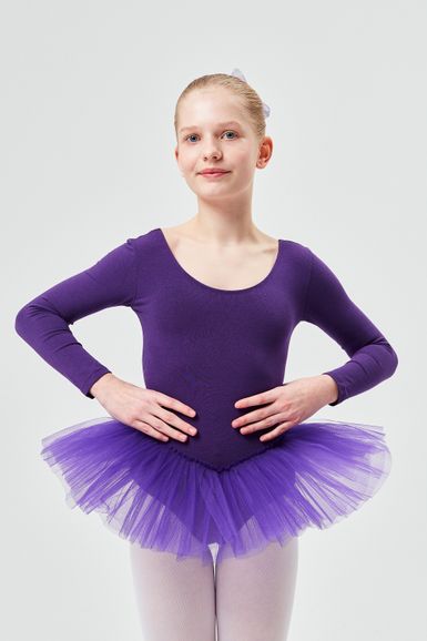 Junge Balletttänzerin in einem lila Ballettbody und Tutu posiert mit den Händen in den Hüften.