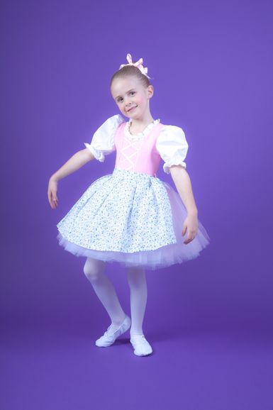Junges Mädchen in einem rosa-blauen Ballettkostüm posiert vor einem schlichten violetten Hintergrund.