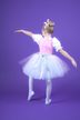 Ein junges Mädchen im Ballettkostüm posiert auf einem Bein vor einem einfarbig violetten Hintergrund 5