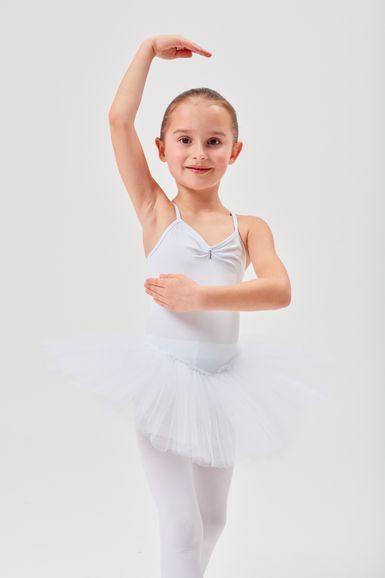 Ein kleines Kind in einem weißen Ballett-Outfit posiert mit einem erhobenen Arm.