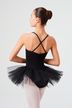 Eine Balletttänzerin in einem schwarzen Ballettbody und Tutu steht mit in die Hüften gestemmten Armen und blickt von der Kamera weg. 2
