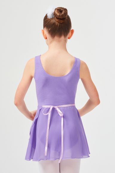 Ein junges Mädchen mit braunem Haar im Dutt trägt ein lavendelfarbenes Ballettbodykleid und steht mit dem Rücken zur Kamera.