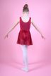 Junges Mädchen in einem roten Ballettbody und Rock mit weißen Strumpfhosen posiert in einer Balletthaltung vor einem rosa Hintergrund. 3