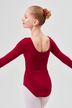 Eine junge Balletttänzerin in einem roten Ballettbody und weißen Strumpfhosen steht mit ausgestreckten Armen da und blickt leicht weg. 2