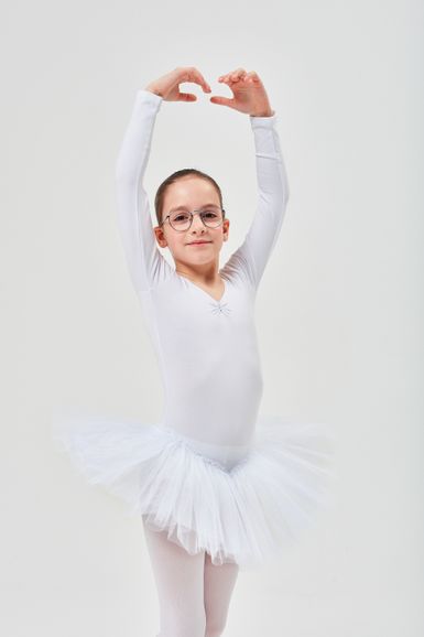 Ein junges Mädchen in einem weißen Ballettkostüm und posiert mit erhobenen Armen.