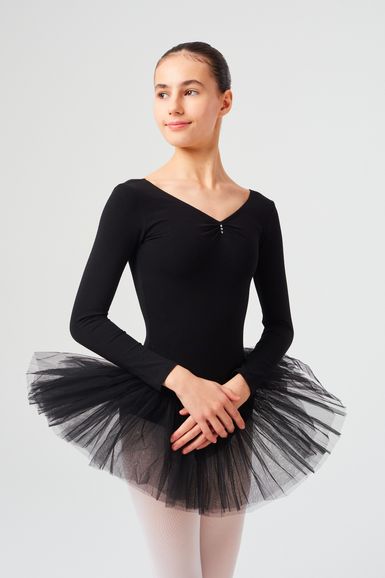 Eine junge Ballerina in einem schwarzen Ballettbody und Tutu steht mit gefalteten Händen und blickt zur Seite.