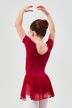 Ein junges Mädchen in einem roten Ballett Trikot und Tutu steht mit erhobenen Armen in einer Ballettpose und blickt von der Kamera weg. 2
